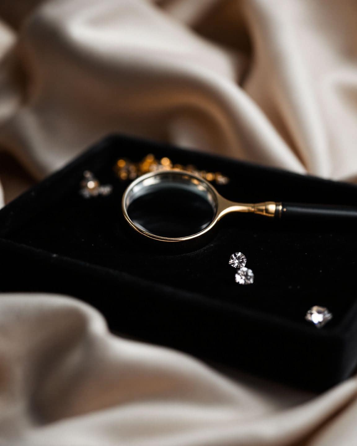A magnifying loupe on a black velvet tray beside several loose diamonds.